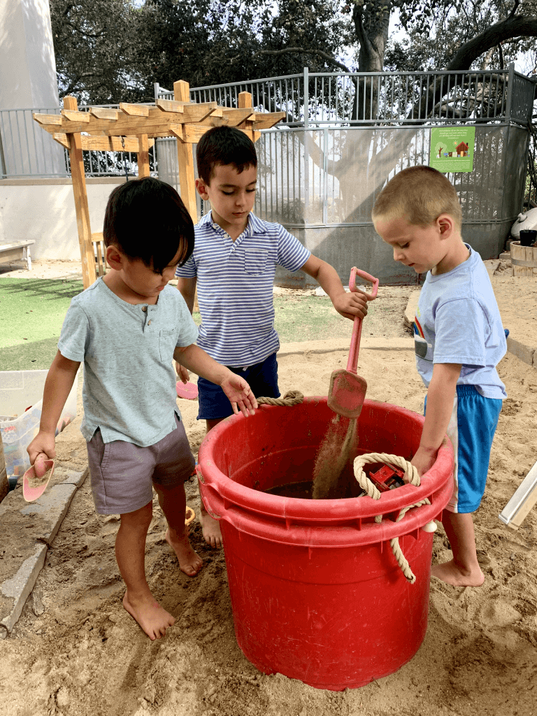 Preschool kids digging in sand and filling a bucket with sand
